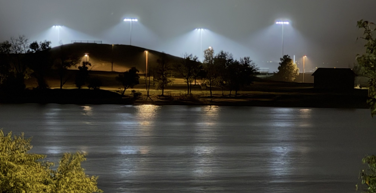 Sports field LED lights glowing at night, reflected on a lake